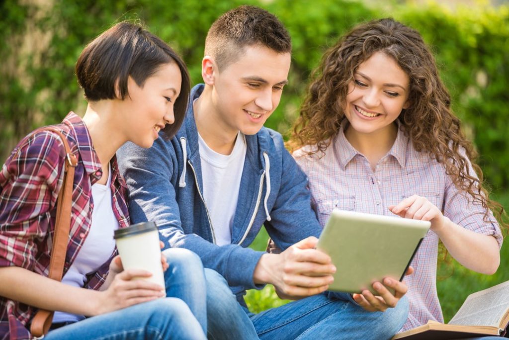 Étudiants révisant ensemble sur une tablette en extérieur près d'un logement étudiant à Rouen